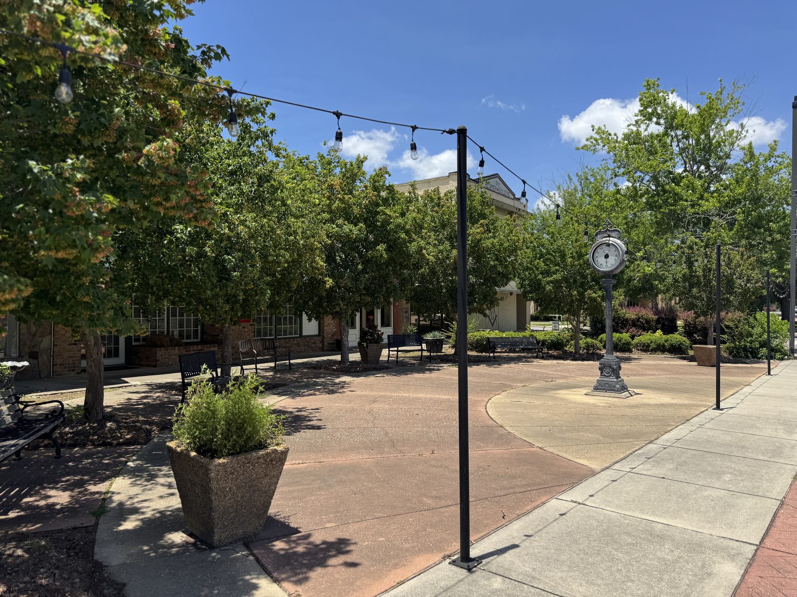 The downtown Moss Point plaza with string lights, shade trees, benches, and a vintage street clock.