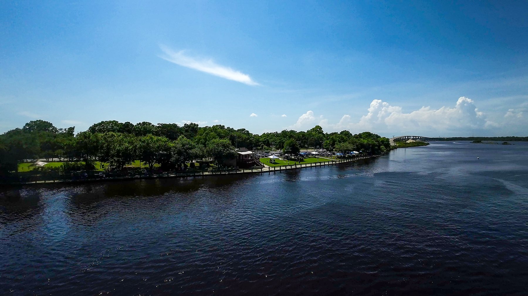 An aerial view of the wide Escatawpa River curving past the tree-lined Moss Point riverfront under a big sky.