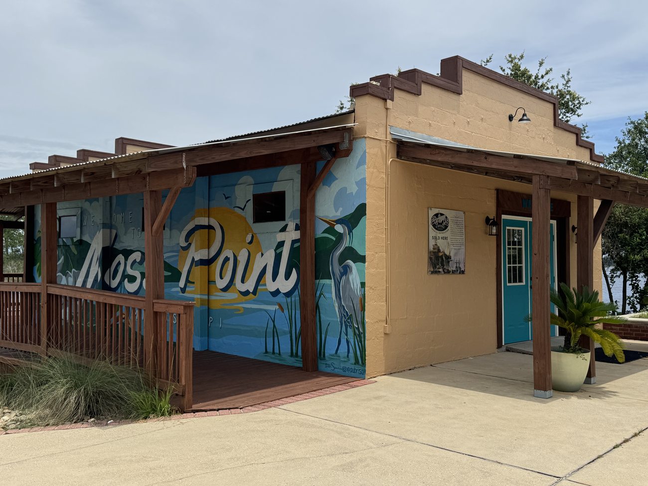 The Moss Point Welcome Center, a small building painted with a mural of the marsh, a great blue heron, and the sun, with Moss Point in script.