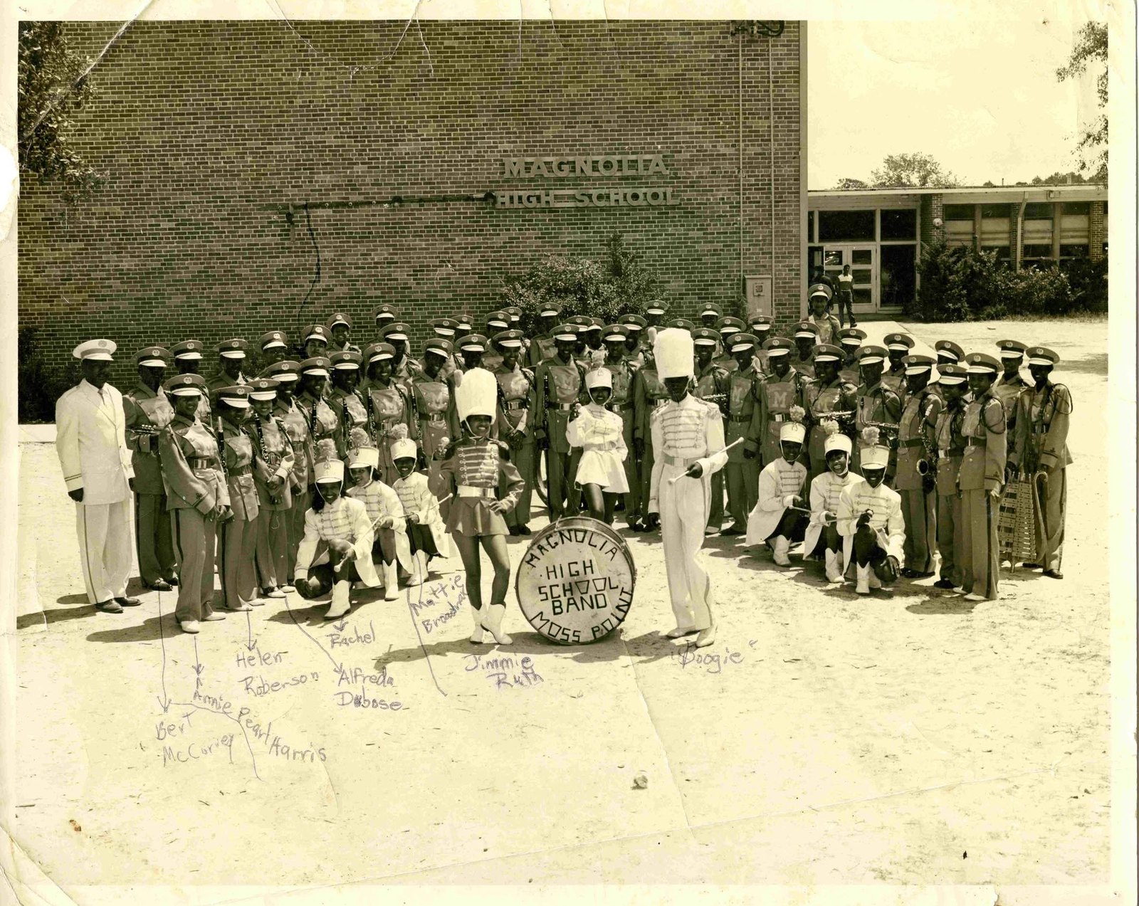 Members of the Magnolia High School marching band in uniform pose in front of the school in Moss Point, the bass drum lettered Magnolia High School Band.