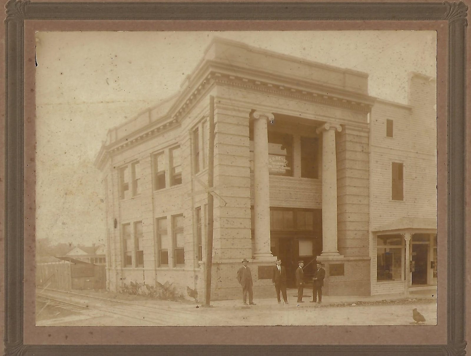 A two-story columned brick bank building on a Moss Point corner with four men standing out front, 1907.