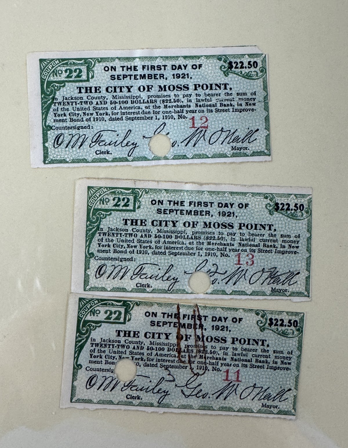 Three green 1910 City of Moss Point street improvement bond coupons of twenty two dollars and fifty cents each, every one punched through the center.