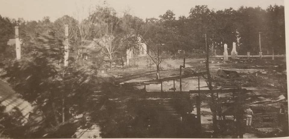 A wide view of smoldering ruins and standing brick chimneys across the burned Moss Point downtown after the 1923 fire.