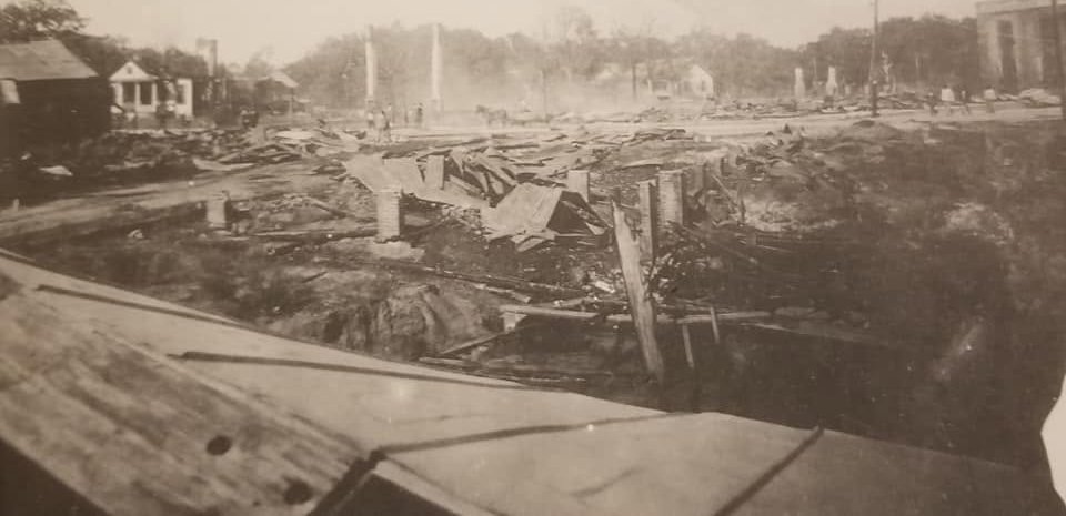 Collapsed roofing and bare brick chimneys among the ruins of downtown Moss Point after the 1923 fire, with people in the distance.