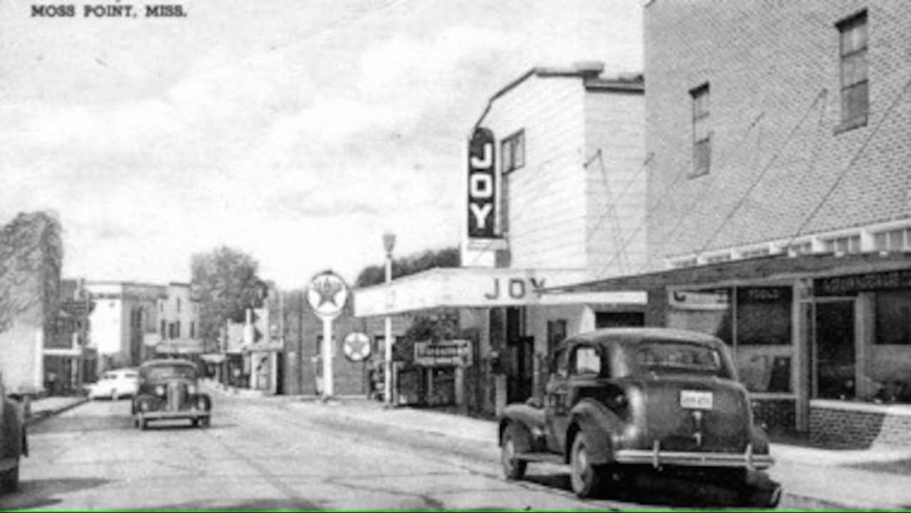 A vintage postcard of Main Street in Moss Point showing the Joy Theatre marquee, a Texaco service station, and 1940s automobiles.