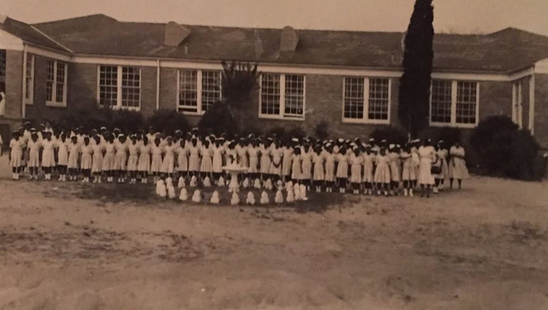 The long brick Magnolia High School building of the 1950s with the school’s 4-H Club, dozens of girls in white dresses, lined up in front.