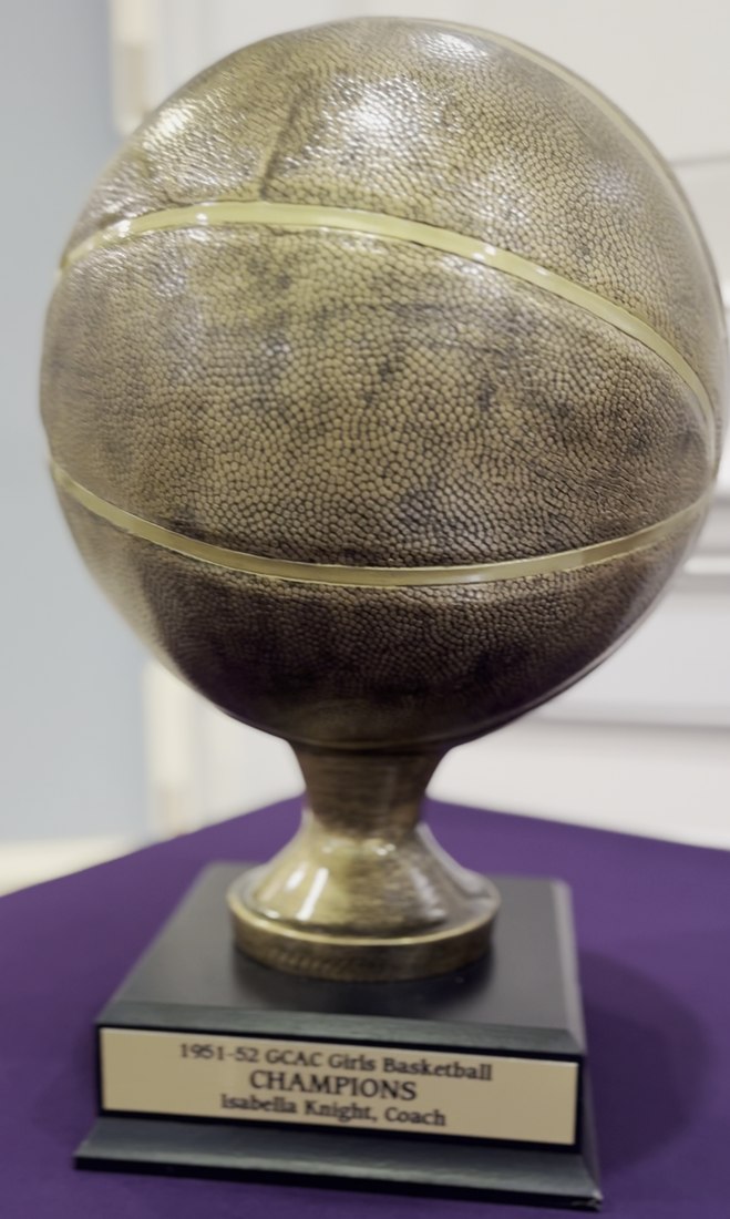 A gold trophy in the shape of a basketball on a stand, its plaque reading 1951 to 1952 GCAC Girls Basketball Champions, Isabella Knight, coach.