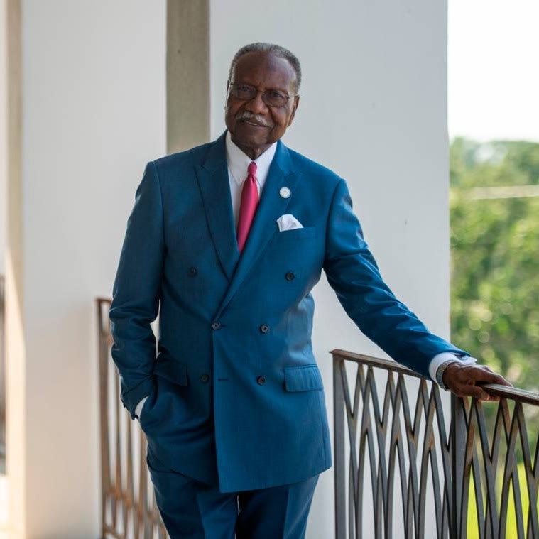 Mayor Billy Knight Sr. in a blue suit standing on a balcony with an iron railing.