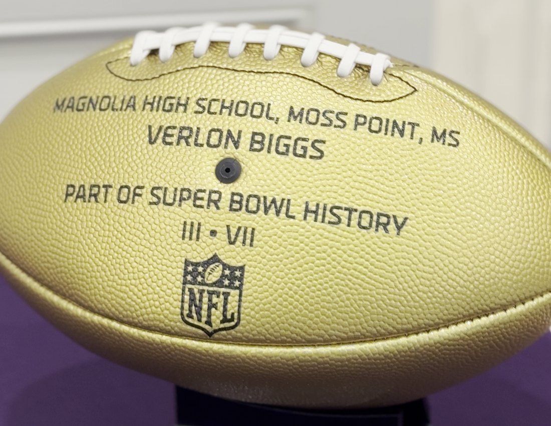 A gold commemorative NFL football reading Magnolia High School, Moss Point, MS, Verlon Biggs, part of Super Bowl history, three and seven.