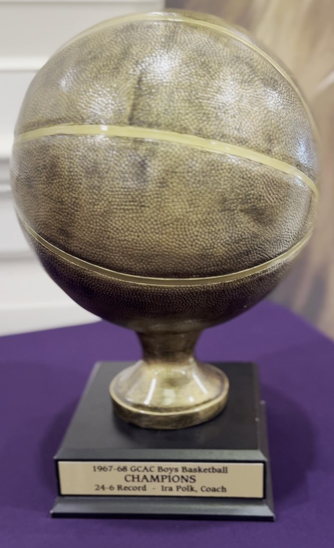 A gold trophy basketball on a stand, its plaque reading 1967 to 1968 GCAC Boys Basketball Champions, 24 and 6 record, Ira Polk, coach.