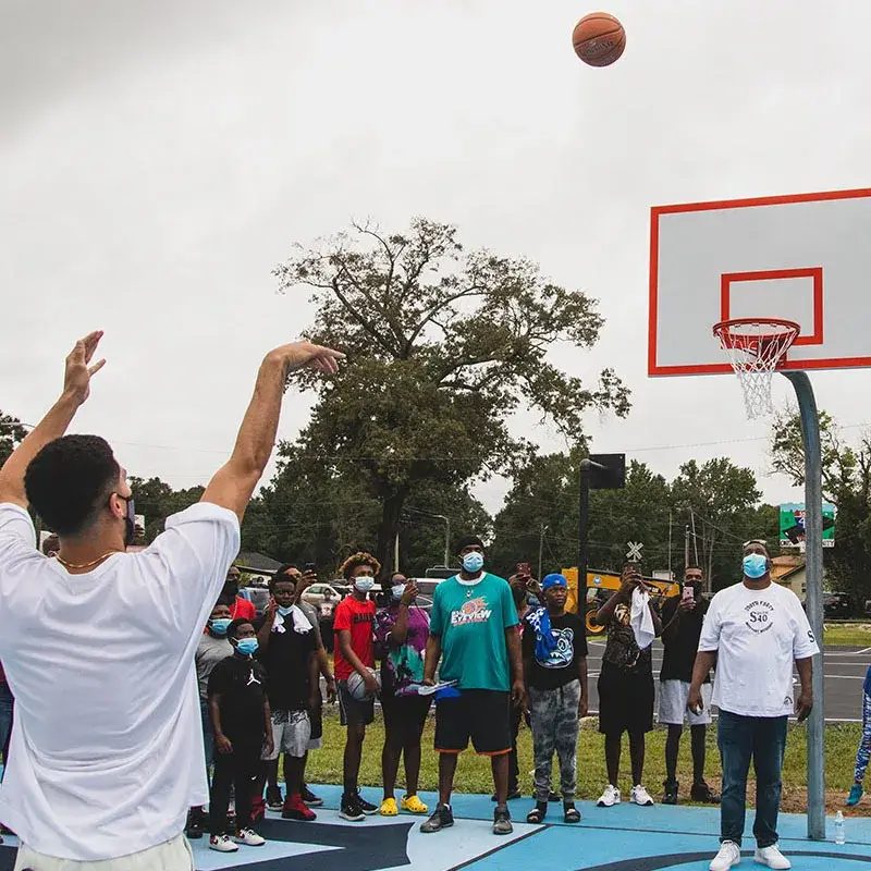 Devin Booker shoots a basketball on the new court while neighborhood kids watch from the baseline.