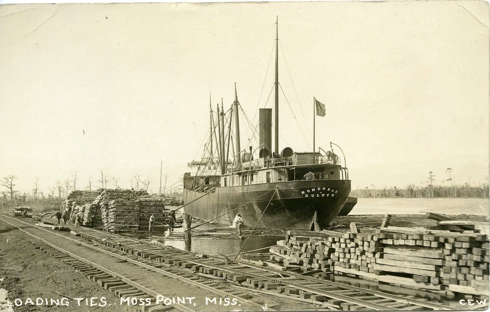 A steamer is loaded with stacked railroad ties beside the rail tracks at the Moss Point waterfront.