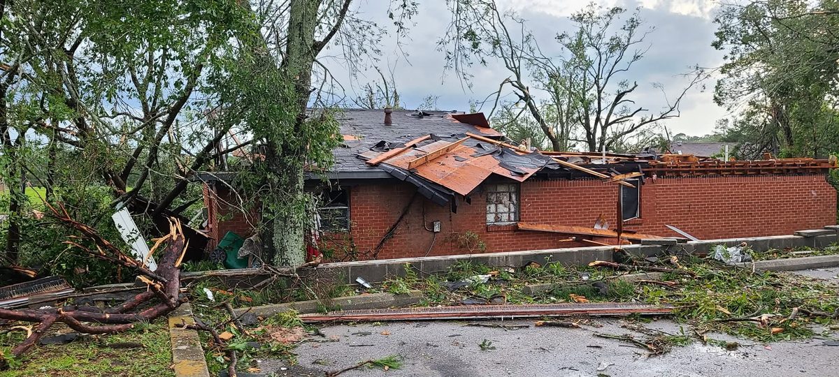 A single-story brick home in Moss Point with its roof torn open and trees down across the yard after the tornado.