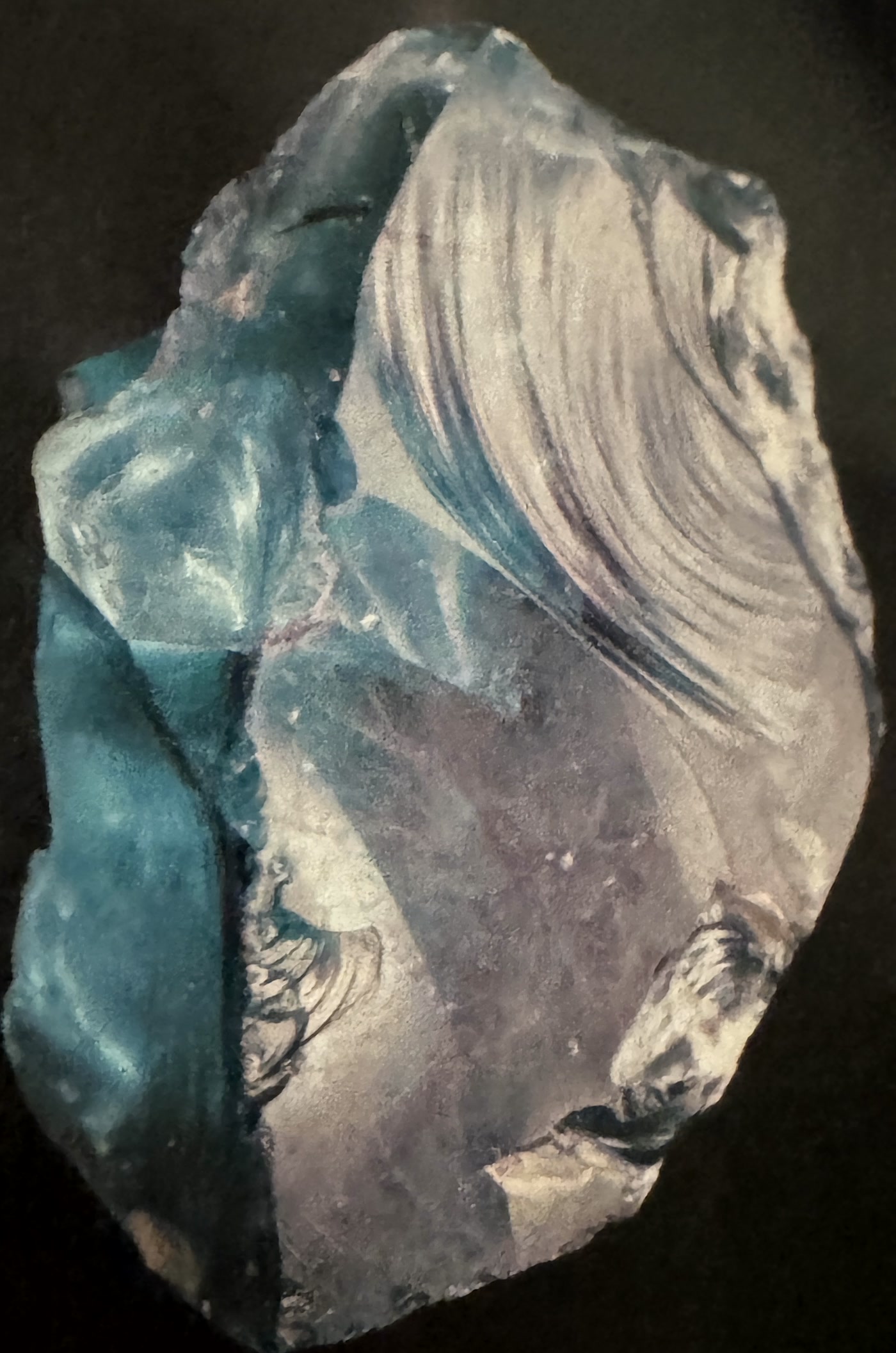 A chunk of translucent blue slag glass photographed against black, its surface rippled and swirled where it melted.