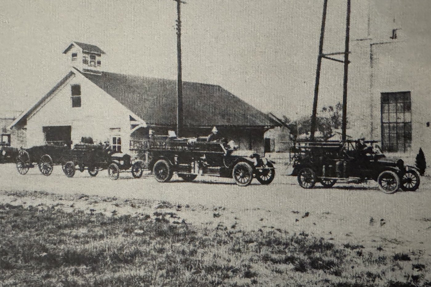 An early photograph of the Moss Point Fire Department, motor fire engines with ladders and helmeted firemen lined up outside a white wooden station with a cupola.
