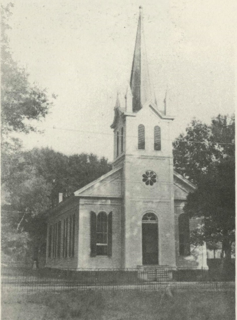 The white frame Moss Point Methodist Church erected in 1882, a tall steeple over an arched entrance, framed by trees.