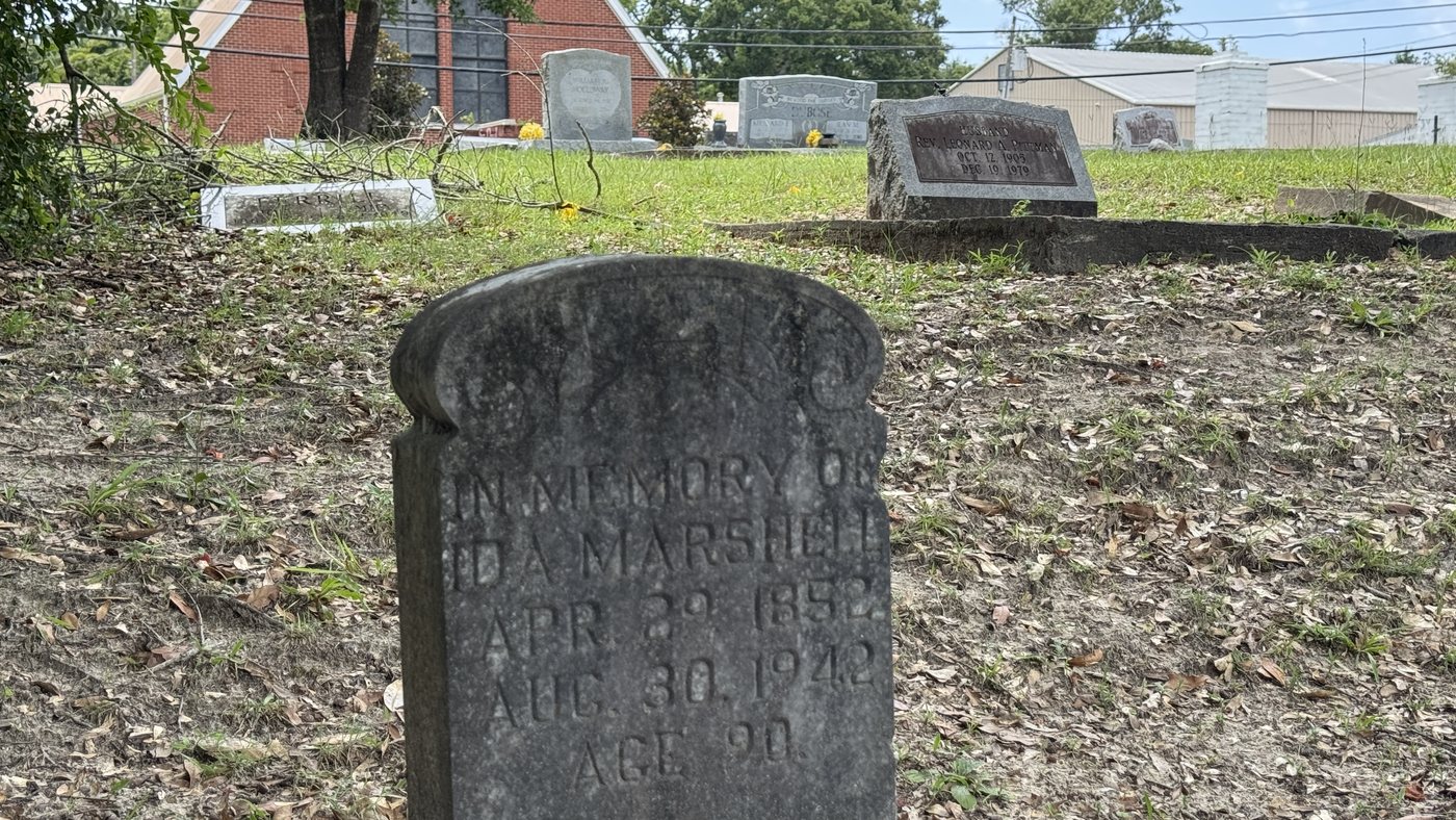 A small weathered headstone reading In Memory of Ida Marshell, April 1852 to August 30, 1942, age 90, with the brick sanctuary of St. Paul United Methodist Church beyond.