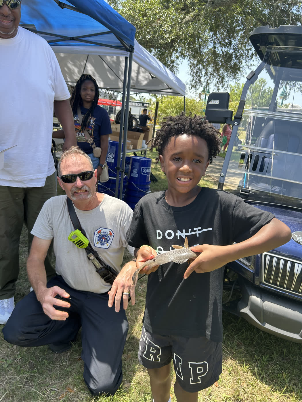 A Moss Point firefighter kneels beside a young angler holding his catch at the Faith Fest Fishing Rodeo