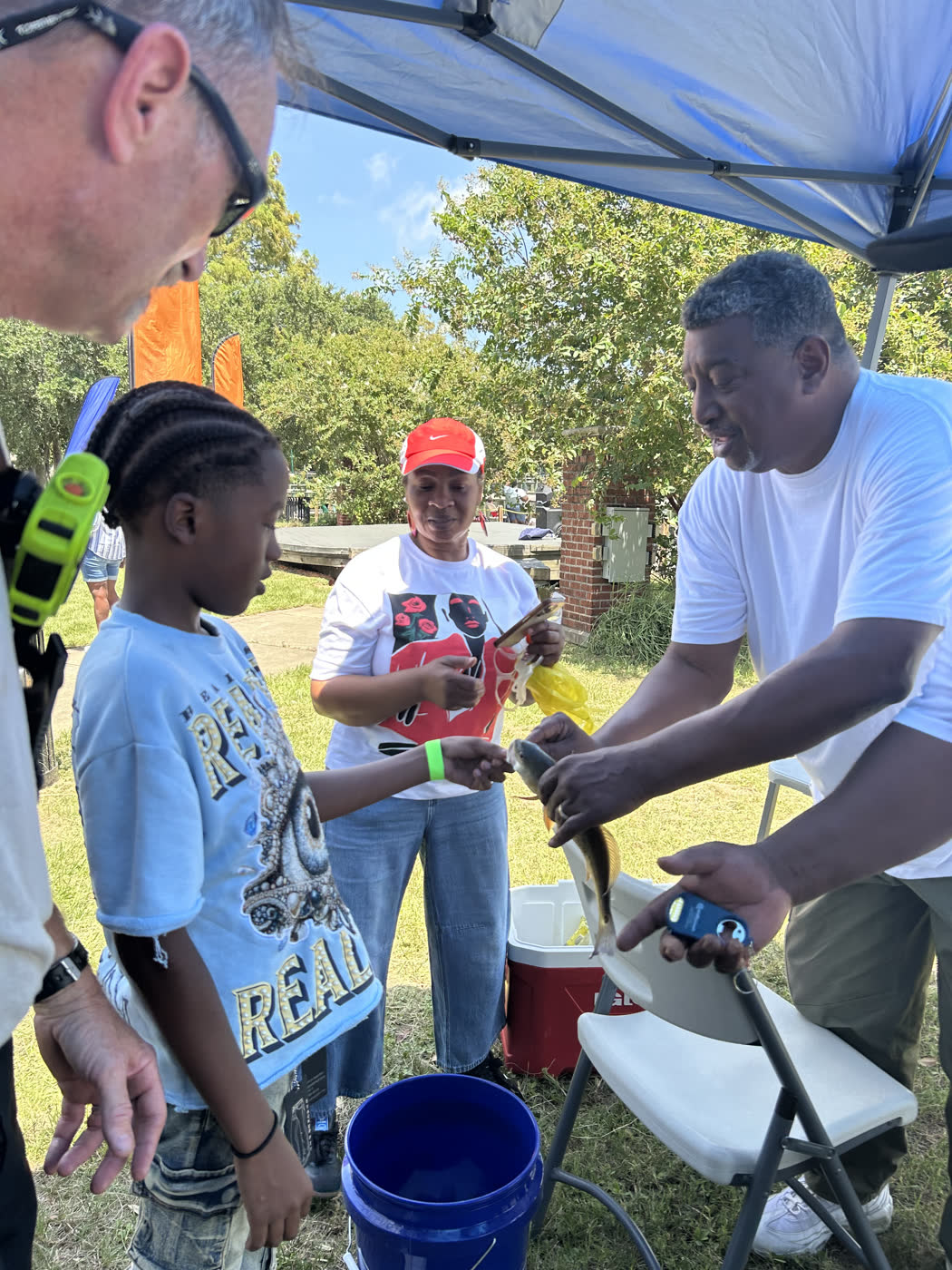 Volunteers help a young angler hand over his fish at the weigh station during the Faith Fest Fishing Rodeo